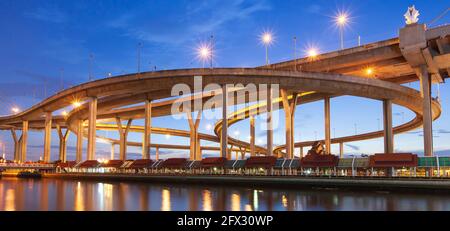 Vue pittoresque à angle bas de l'échangeur de l'autoroute et des ponts suspendus au crépuscule, des lumières lumineuses se reflètent sur la rivière Chao Phraya, en Thaïlande. Banque D'Images