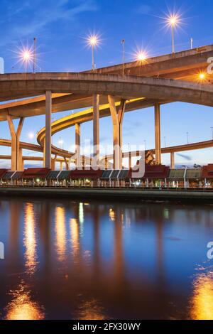 Vue pittoresque à angle bas de l'échangeur de l'autoroute et des ponts suspendus au crépuscule, des lumières lumineuses se reflètent sur la rivière Chao Phraya, en Thaïlande. Banque D'Images