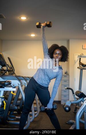 Femme lever des haltères à la salle de gym à la maison. Gros plan, une personne, modèle de fitness, afro-américain, modèle africain, sportswear, modèle de cheveux naturels, fond, bl Banque D'Images