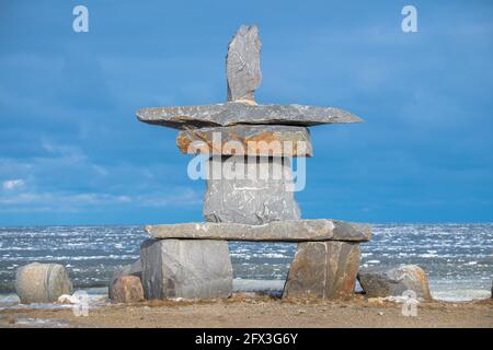 Un grand Inukshuk qui se trouve sur le rivage de la baie d'Hudson, à Churchill, au Manitoba, dans le nord du Canada. Glace de mer glacée en arrière-plan et ciel bleu. Banque D'Images