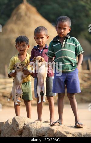 LANJIA SAORA TRIBE - les enfants posant pour caméra avec leurs chiots de compagnie. Village tribal de Puttasingh, Odisha, Inde Banque D'Images