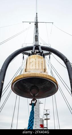 Cloche du navire d'or avec corde bleue contre le mât et ciel gris, Banque D'Images