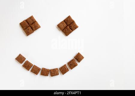 céréales muesli petit-déjeuner en forme de visage souriant sur fond blanc, la nourriture et le concept de style de vie, oreillers en chocolat avec espace pour le texte, haut Banque D'Images