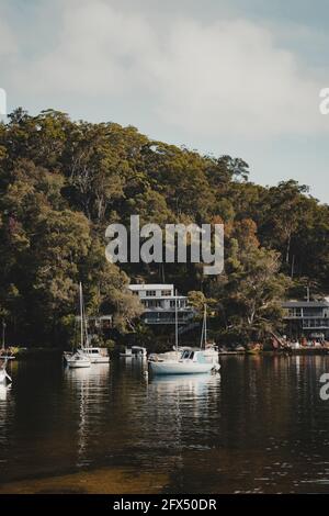 Bateaux sur l'eau devant des maisons idylliques en bord de mer à Berowra Waters, Nouvelle-Galles du Sud. Comme vu de la Great North Walk. Banque D'Images