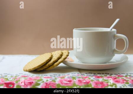Gros plan d'une table où il y a des biscuits à côté d'une tasse de boisson chaude, sur un tapis fleuri, avec un espace pour copier Banque D'Images