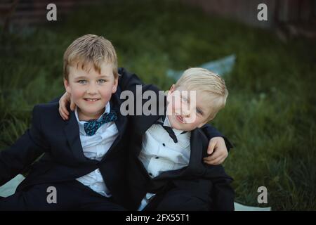 Adorables garçons australiens portant des costumes noirs et embrassant les autres sur l'herbe Banque D'Images