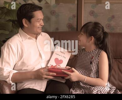 Petites filles asiatiques félicitant papa et lui donnant la carte postale Et boîte cadeau avec sourire et embrassant.concept de père heureux jour Banque D'Images