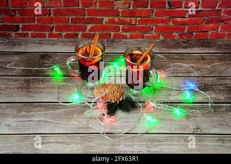 Deux verres de vin chaud aux épices, une pinecone avec une pile de lumières de Noël sur une table contre un mur de briques. Gros plan. Banque D'Images