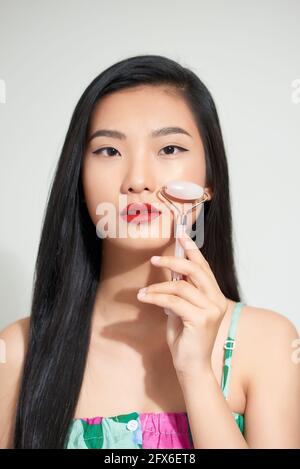 Femme saine de peau utilisant un rouleau de visage de quartz rose sur sa peau impeccable. Banque D'Images