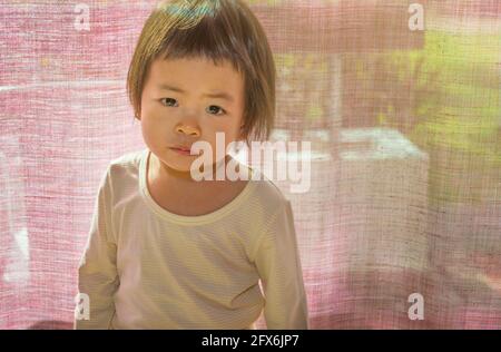 Portrait d'une jeune fille asiatique debout devant un rideau, lumière vive de derrière, yeux regardant directement l'appareil photo, espace vide pour la copie et la recherche Banque D'Images