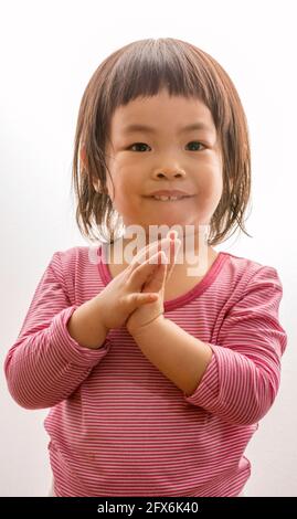 Portrait mignon asiatique ou thaï petite fille sur fond blanc, un enfant essayant de saluer dans la culture de Thaïlande en mis les deux mains ensemble ou être appelé Sawat Banque D'Images