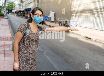 Une touriste asiatique salue un taxi dans la ville de Bangkok en Thaïlande, une femme portant un masque médical dans la rue le matin. Banque D'Images