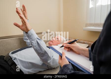 Un homme âgé se trouve sur un canapé et tient ses mains pendre pendant un rendez-vous avec un hypnothérapeute. Un homme âgé dans un individu Banque D'Images