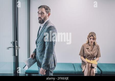 Homme inquiet entrant dans le bureau et femme en attente Banque D'Images