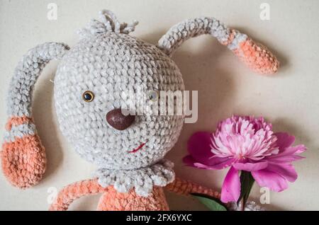 Lièvre crocheté avec fleur de pivoine rose sur fond de bois. Jouet fait main Banque D'Images