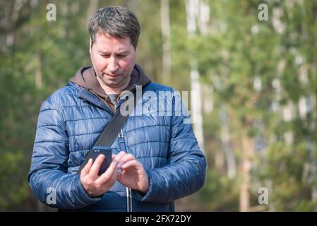 Un homme de 40s avec son smartphone mobile à la recherche du signal de réception dans la forêt de printemps. Banque D'Images