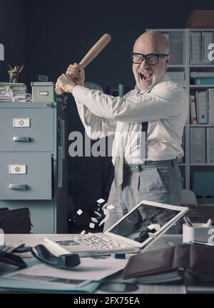 Un homme d'affaires fou stressé détruisant son bureau et son ordinateur portable avec une batte de baseball, le concept de l'épuisement professionnel Banque D'Images