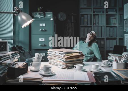 Employé de bureau épuisé qui s'est endormi dans le bureau tard à nuit après avoir bu trop de café Banque D'Images