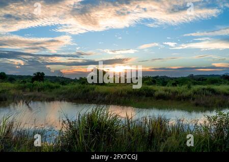 Vue panoramique du magnifique coucher de soleil au-dessus du lac en été ciel nuageux et champ d'herbe. Paysage de coucher de soleil et ciel bleu réfléchi sur l'eau Banque D'Images