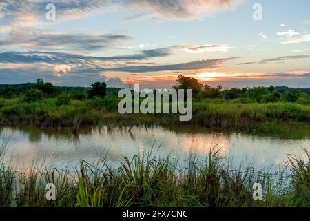 Vue panoramique du magnifique coucher de soleil au-dessus du lac en été ciel nuageux et champ d'herbe. Paysage de coucher de soleil et ciel bleu réfléchi sur l'eau Banque D'Images