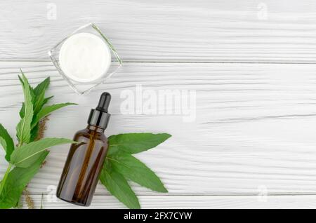 Crème, herbes et une bouteille de verre sombre sur un fond en bois clair. Flat lay, vue de dessus, espace de copie. Concept de soins de la peau et de soins de beauté Banque D'Images