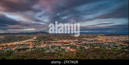 Une vue aérienne depuis le sommet de Castle Hill de la ville du côté ouest s'étend éclairée par les lumières de la rue à l'heure bleue à Townsville, Queensland, Australie. Banque D'Images