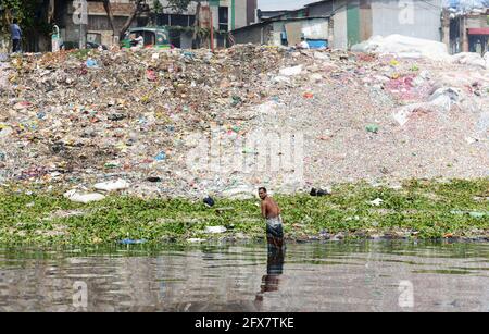 Un bangladais se lavant par un tas de déchets sur les rives du fleuve Buriganga à Dhaka, au Bangladesh. Banque D'Images