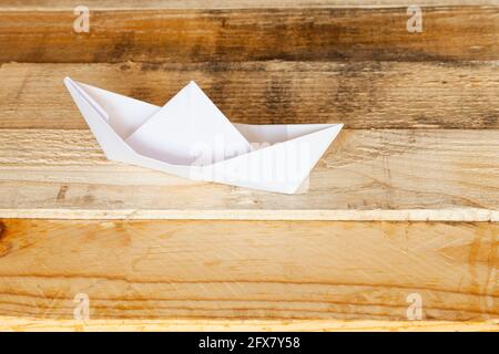 Bateau origami isolé sur une surface en bois. Le véhicule est en papier blanc. Banque D'Images