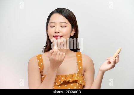 Portrait gai belle jeune femme posant avec le rouge à lèvres rose et la brosse mascara dans les mains et sourire isolé fond blanc. Banque D'Images