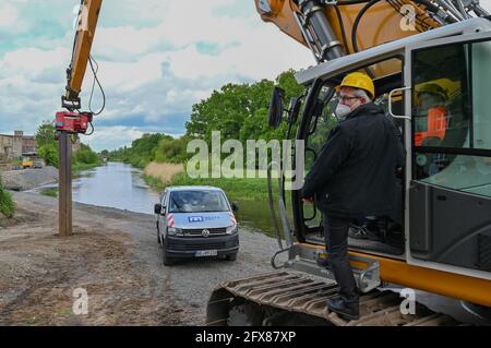 26 mai 2021, Brandebourg, Guben: Axel Vogel (Bündnis 90/Die Grünen), Ministre de l'agriculture, de l'environnement et du climat de l'État de Brandebourg, brise symboliquement le sol sur une pelle avec un conducteur de pile pour l'extension de la protection contre les inondations sur la rivière frontière Neisse. Cela permettra d'améliorer encore la protection contre les inondations dans la ville. À l'heure actuelle, la digue existante et le mur de remblai dans la zone du Plastinarium, qui a grand besoin de rénovation, ne fournissent pas une protection suffisante contre les inondations pour la zone urbaine de Guben dans la zone d'Alte Poststraße avec la hauteur actuelle de la cime. Po Banque D'Images