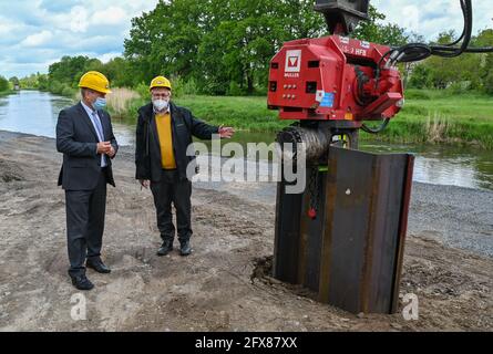 26 mai 2021, Brandebourg, Guben: Fred Mahro (l., CDU), Maire de Guben, Et Axel Vogel (Bündnis 90/Die Grünen), ministre de l'Agriculture, de l'Environnement et du climat de l'État de Brandebourg, se tiennent à côté d'un conducteur de pieux avec un mur de pieux en tôle d'acier pour la cérémonie révolutionnaire d'expansion de la protection contre les inondations sur la rivière frontière Neisse. Cela permettra d'améliorer encore la protection contre les inondations dans la ville. À l'heure actuelle, la digue existante et le mur de remblai dans la région du Plastinarium, qui a grand besoin d'être rénovés, ne fournissent pas une protection suffisante contre les inondations dans la zone urbaine de Gu Banque D'Images