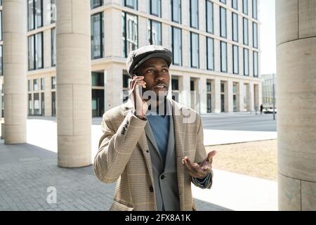 Un jeune homme africain parle sur un téléphone portable tout en restant debout la ville Banque D'Images
