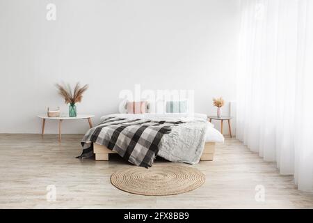 Lit avec oreillers et couverture, moquette ronde, tables avec plantes sèches dans des vases sur parquet Banque D'Images