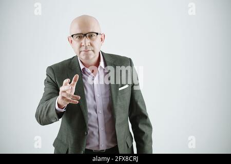 Portrait d'un curieux homme d'affaires blanc chauve en lunettes debout contre arrière-plan gris et gestuelle lors de l'utilisation d'un tableau interactif Banque D'Images