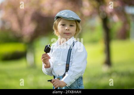 Mode enfant tout-petit, manger de la crème glacée et pousser les enfants poussette avec poupée tricotée dans lui dans le parc Banque D'Images