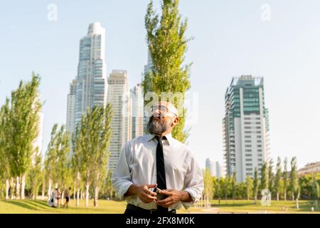 Homme d'affaires asiatique confiant dans un parc en face de gratte-ciel. Banque D'Images