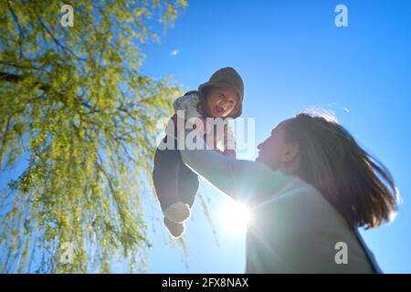 Silhouette de mère et de bébé au coucher du soleil. La mère jette l'enfant dans les airs. Banque D'Images