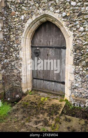 Une ancienne porte voûtée en chêne avec de longues charnières boulonnées Un mur de pierre à une église dans le centre de Norfolk Angleterre Banque D'Images
