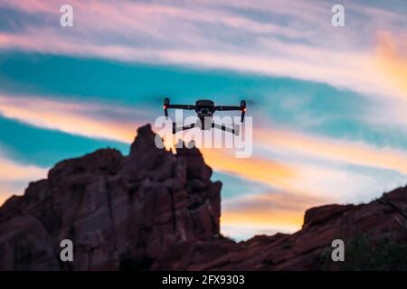 Gros plan d'un drone volant sous un ciel nuageux au coucher du soleil sur un fond montagneux Banque D'Images