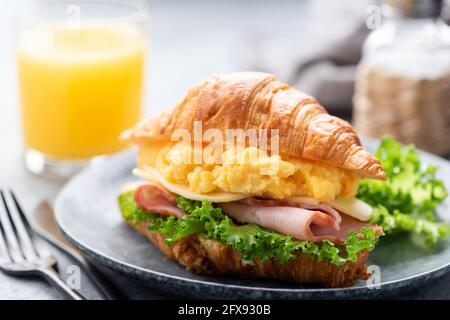 Sandwich croissant avec jambon, fromage, œufs brouillés pour le petit déjeuner servi avec un verre de jus d'orange Banque D'Images