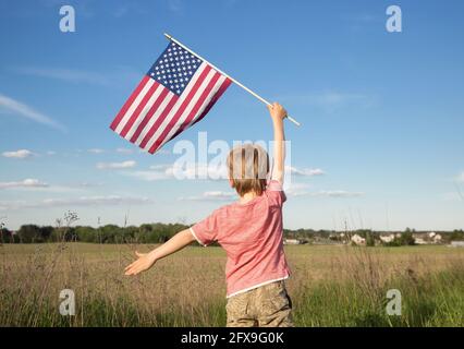 Drapeau américain dans la main d'un enfant garçon debout avec son dos contre le fond du champ. Jour de l'indépendance des États-Unis d'Amérique Banque D'Images