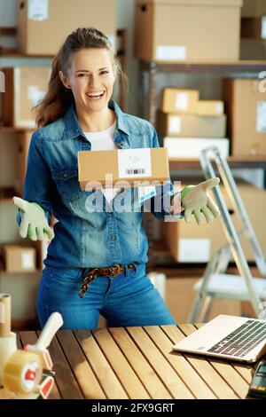 Entreprise de livraison. Femme moderne heureuse en jeans avec colis dans l'entrepôt. Banque D'Images