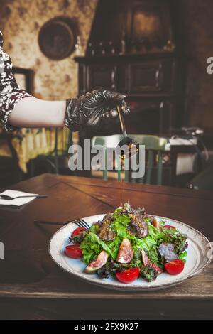 Salade d'arugula et d'épinards avec foie de poulet, tranches de figues et une délicieuse sauce. La sauce est versée à partir d'une cuillère dorée sur la salade. Banque D'Images