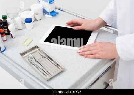 vue rognée des mains de dentiste femelle à l'aide d'une tablette avec blanc écran près des outils dentaires métalliques dans le plateau Banque D'Images