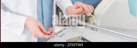 vue rognée des mains de dentiste femelle tenant des outils métalliques au-dessus du plateau métallique sur la table dans la clinique dentaire, bannière Banque D'Images