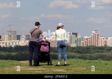 Couple avec bébé bébé en marche au sommet d'une colline sur fond de ville d'été et de bâtiments en construction. Loisirs en famille, planification future Banque D'Images