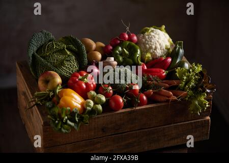 Caisse en bois avec assortiment de légumes frais placée sur fond sombre dans une pièce sombre Banque D'Images