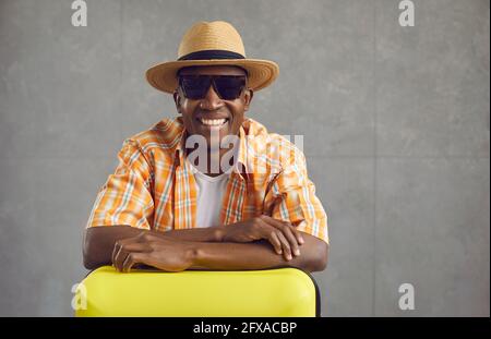 Studio portrait de touriste noir heureux en chapeau et lunettes de soleil avec sa valise de voyage Banque D'Images