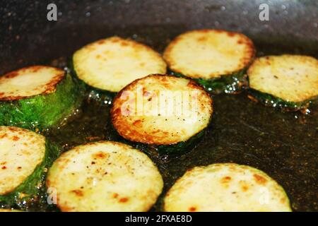 Gros plan de courgettes émincées friture à l'huile d'olive, dans une poêle. Banque D'Images