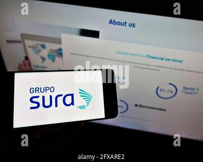 Personne tenant un smartphone avec le logo de la société colombienne de services financiers Grupo Sura sur l'écran devant le site. Mise au point sur l'affichage du téléphone. Banque D'Images